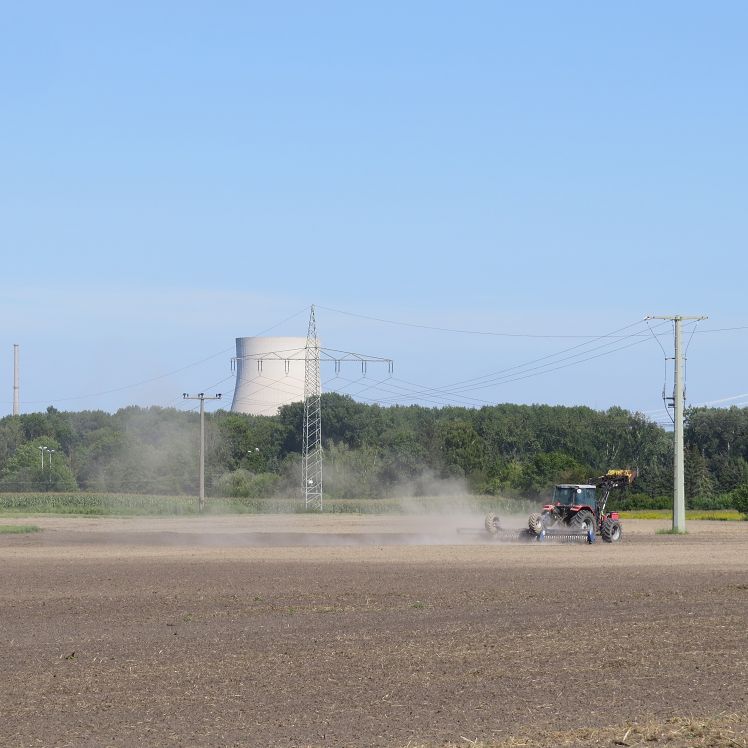 Kühlturm des ehemaligen AKW Niederaichbach - davor ein Feld, das gerade bearbeitet wird